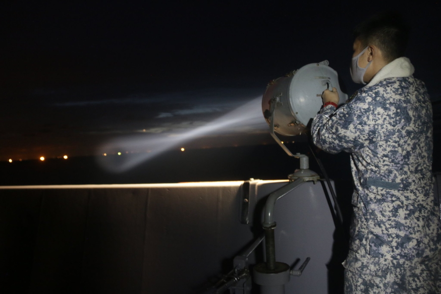 "LOOK FORWARD TO BRIGHTER DAYS AHEAD AND STRONGER COOPERATION AT SEA." During the flashing exercise (FLASHEX), a communication systems operator uses the signal lantern to send a message in morse code to USS Gabrielle Giffords.